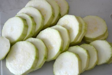 Healthy food, vegetables, peeled zucchini cut into rings and cubes are located on a white kitchen plastic board.