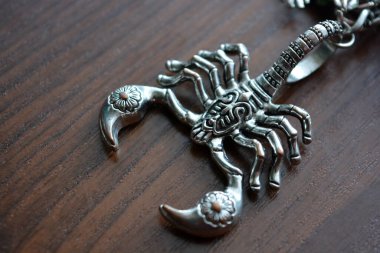 A small metal scorpion with carved ornaments is placed on a brown wooden table.