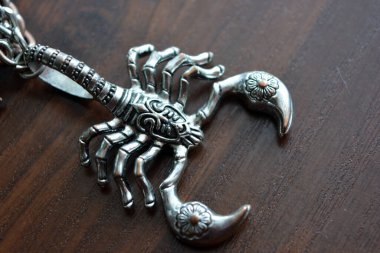 A small metal scorpion with carved ornaments is placed on a brown wooden table.