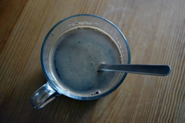 Fresh delicious black brewed coffee is poured into a glass cup and placed on a wooden table.