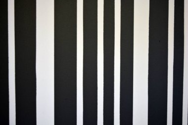 Graphic building background consisting of black and white stripes of different lengths and thicknesses. Striped wall painted with matte paint, unusual graphics and texture.