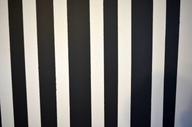 Graphic building background consisting of black and white stripes of different lengths and thicknesses. Striped wall painted with matte paint, unusual graphics and texture.
