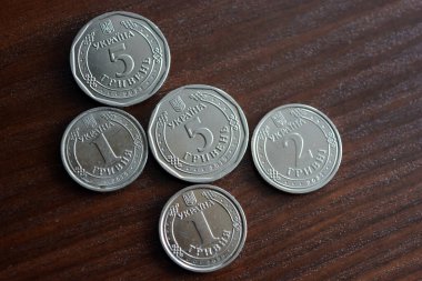 Ukrainian kopecks, small change in the amount of one 1, two 2, five 5 hryvnias are located on a dark brown table.