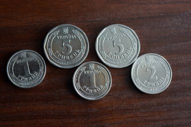Ukrainian kopecks, small change in the amount of one 1, two 2, five 5 hryvnias are located on a dark brown table.