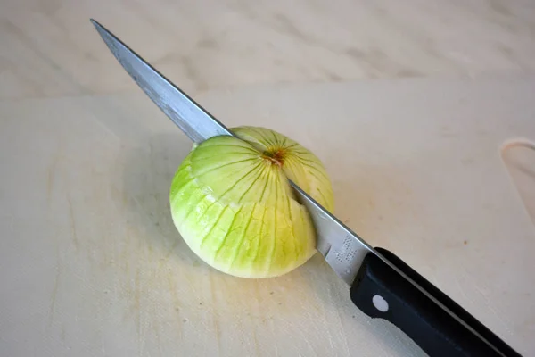 A large white green onion and a utility knife with a black handle lie on a white plastic board. Cooking products for soup, chives onion, chopped onion, cut onion on the kitchen table.