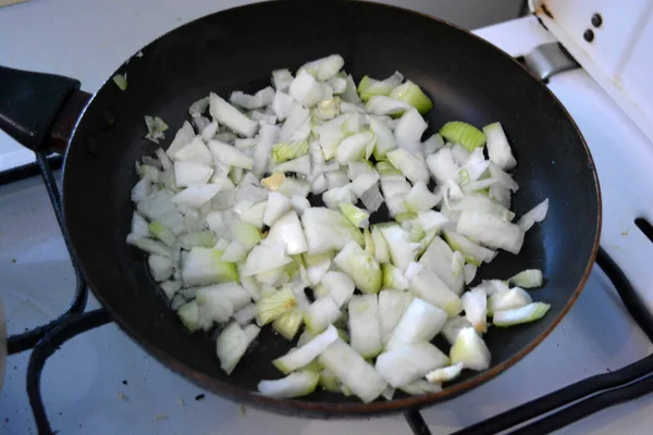 Cooking healthy food, onion is cut into cubes and fried in a black round kitchen pan.