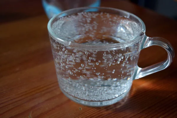 One glass coffee cup stands with mineral water on a brown wooden table.