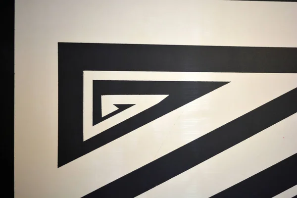 A black and white drawing of stripes of different widths and lengths, consisting of chaotic angles, lines, triangles, applied to a building wall. A graphic background made of textured matte paint.