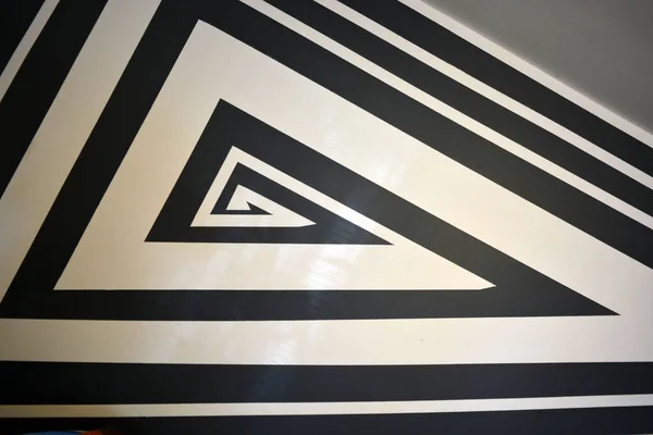 A black and white drawing of stripes of different widths and lengths, consisting of chaotic angles, lines, triangles, applied to a building wall. A graphic background made of textured matte paint.