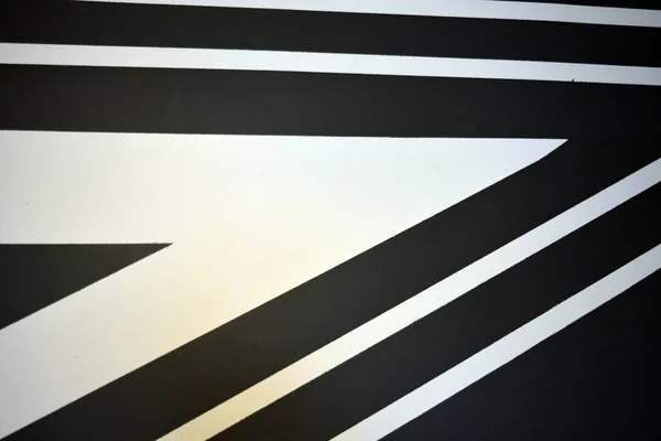 A black and white drawing of stripes of different widths and lengths, consisting of chaotic angles, lines, triangles, applied to a building wall. A graphic background made of textured matte paint.