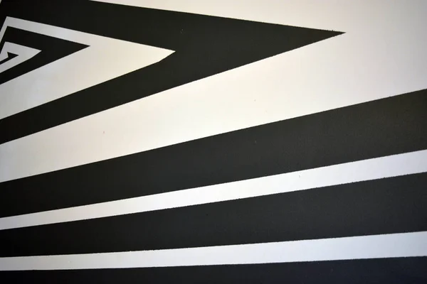 A black and white drawing of stripes of different widths and lengths, consisting of chaotic angles, lines, triangles, applied to a building wall. A graphic background made of textured matte paint.