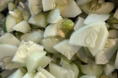 Bir sürü dilimlenmiş çeyrek salatalık büyük beyaz bir salata kasesine istiflenmiş. Faydalı sebzeler, sağlıklı yiyecekler, dilimlenmiş tohumlu salatalıklar..