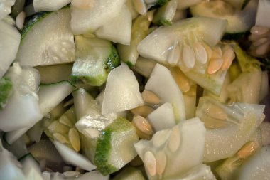 Bir sürü dilimlenmiş çeyrek salatalık büyük beyaz bir salata kasesine istiflenmiş. Faydalı sebzeler, sağlıklı yiyecekler, dilimlenmiş tohumlu salatalıklar..