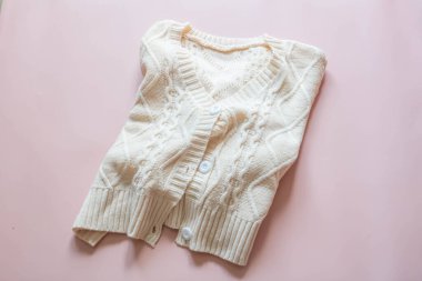 Top view of a white knitted sweater on a pink background.