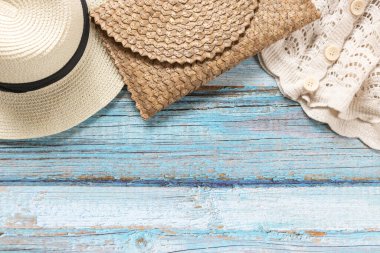 Hasır şapka, açık mavi ahşap arka planda beyaz örgü gömlekli hasır çanta. Plaj ve Yaz konsepti.