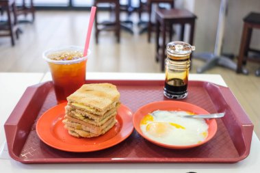 Kaya tostu, tereyağlı tost ve kaya, buzlu çay ve kaynamış yumurta ile servis edilir..