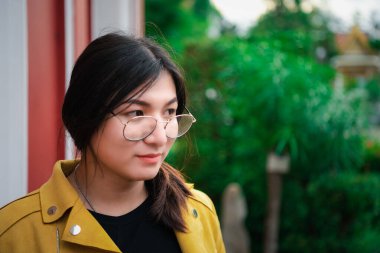 Güzel Asyalı kadın (LGBTQ) doğal makyaj, moda sarı deri kıyafetler ve gözlüklerle eski kentte ve klasik bina modasında poz verir.