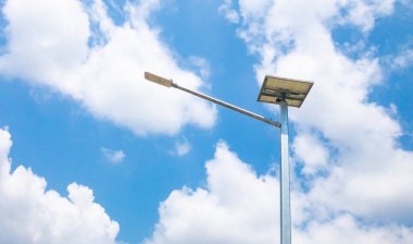 Gün boyunca aydınlatılmış bir lamba direği resmi güneş panellerinden gelen güneş jeneratörlerini parlak beyaz bulutlu mavi gökyüzüne karşı temiz enerji olarak kullanıyor..