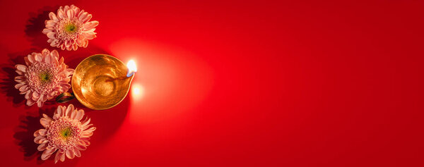 Happy Diwali. Diya oil lamp and flowers on red background. Traditional Hindu celebration. Religious holiday of light. Copy space, banner format.