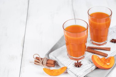 Beyaz ahşap arka planda iki bardak balkabağı suyu. Sağlıklı beslenme için sebze arıtma içeceği. Vejetaryen içeceği. Boşluğu kopyala.