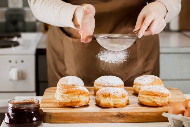 Kadın ev mutfağında reçelli taze çörek hazırlıyor. Geleneksel Yahudi Hannuka sufganiyotu pişiriyorum. Eller Berlinlilere pudra şekeri serpiyor.