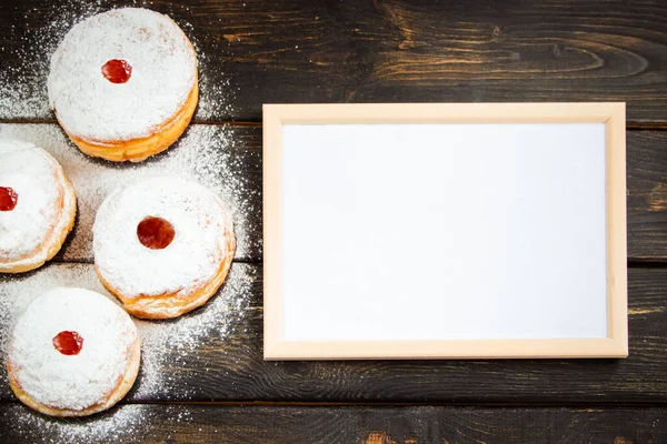 Happy Hanukkah. Empty frame for congratulations text and traditional dessert Sufganiyot on dark wooden background. Celebrating Jewish religious holiday.