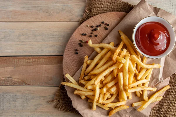 Gorące złote frytki z ketchupem na drewnianym tle. Smaczne amerykańskie fast food. — Zdjęcie stockowe