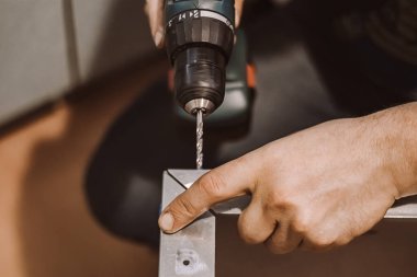 Erkek tamirci, atölyede elektrikli matkapla çalışıyor. İşçi metalde delik açıyor. Yaşam tarzı, profesyonel aktivite. Eller tamir aletini tutar..