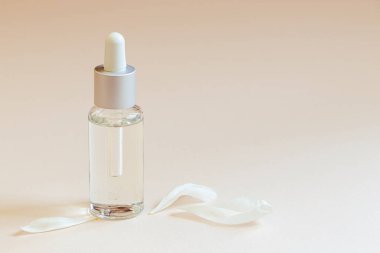 Renkli pastel bej arka planda yüz serumu ve beyaz çiçek yaprakları. Aromatik yağlı doğal kozmetik ürünler. Vücut bakımı için spa ürünü. Boşluğu kopyala.