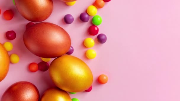 Huevos de Pascua dorados y caramelos sobre fondo rosa. Felices vacaciones de primavera. — Vídeo de stock