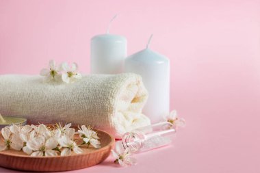 Spa ve aromaterapi için kozmetik ürünler. Mumlar, deniz tuzu, havlu ve pembe arka planda çiçekler. Cilt bakımı ve güzellik kavramı.