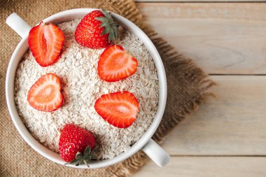 Tahta arka planda yulaf ezmesi ve taze çilek. Sağlıklı bir köy kahvaltısı. Keten peçetede bir kase granola..