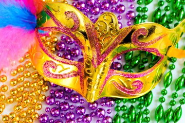 Golden carnival mask and colorful beads close-up. Mardi Gras or Fat Tuesday symbol. Concept of traditional festival. Holiday decorations in gold, green and purple. clipart