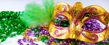 Altın karnaval maskesi ve renkli boncuklar. Mardi Gras veya Fat Tuesday sembolü. Geleneksel festival kavramı. Altın, yeşil ve mor renkli tatil süslemeleri. Sancak biçimi.