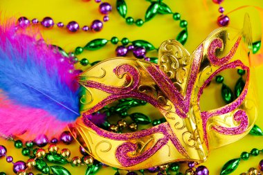 Sarı arka planda tüyleri olan karnaval maskesi. Yeşil, altın ve mor renkli boncuklar. Mardi Gras veya Şişman Salı sembolü.