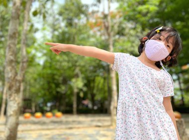 Bahçede maske takan sevimli küçük bir kız.