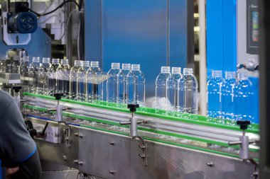 İçme suyu fabrikasındaki işlemleri tamamlamak için konveyör bandındaki boş PET şişeleri. Plastik şişe üretim sürecinin yüksek teknolojisi..