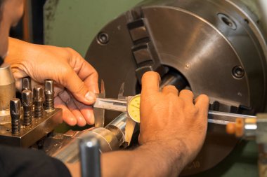 Yakın çekim sahnesi, makine operatörü metal şaft parçalarının çapını Vernier Caliper ile ölçer. Makineyi döndürerek metal işleme süreci.