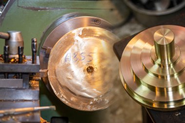 Torna makinesinin pirinç şaft parçalarını kestiği soyut sahne. Makineyi döndürerek metal işleme süreci.