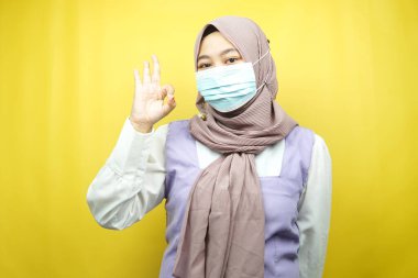 Tıbbi maske takan Müslüman kadınlar, anti-korona virüsü hareketi, covid-19 hareketi, maske takan sağlık hareketi, iyi iş, başarı, zafer, sarı arka planda izole edilmiş eller.
