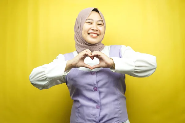 美しいアジアの若いイスラム教徒の女性は 黄色の背景に隔離された胸の上に愛 幸せの手のサインで自信を持って 熱狂的かつ陽気に笑みを浮かべて — ストック写真