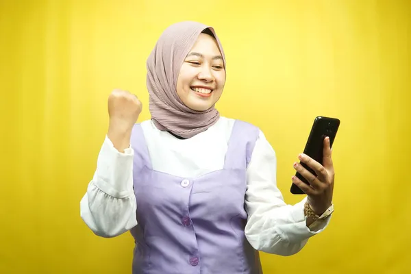 美しい若いアジアのイスラム教徒の女性は 自信に満ちた 熱狂的で明るい笑みを浮かべて手をスマートフォンを保持し 手をきれいに パンチ 良い仕事 黄色の背景に孤立し 広告コンセプト — ストック写真