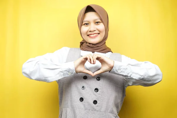 美しいアジアの若いイスラム教徒の女性は 黄色の背景に隔離された胸の上に愛 幸せの手のサインで自信を持って 熱狂的かつ陽気に笑みを浮かべて — ストック写真