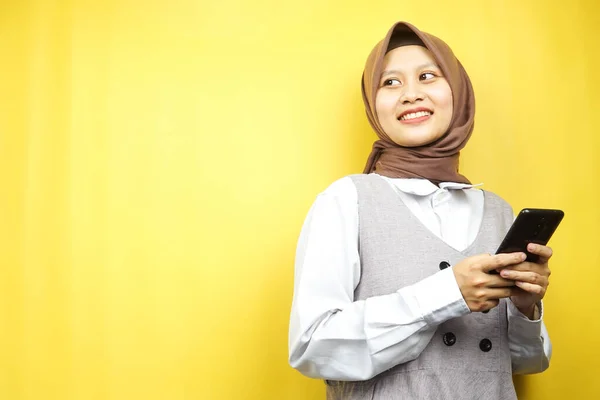 美しい若いアジアのイスラム教徒の女性は自信に満ちて笑顔 スマートフォンを手で熱狂的かつ陽気です 何かを提示空のスペースを見て表示 黄色の背景に隔離されました 広告コンセプト — ストック写真