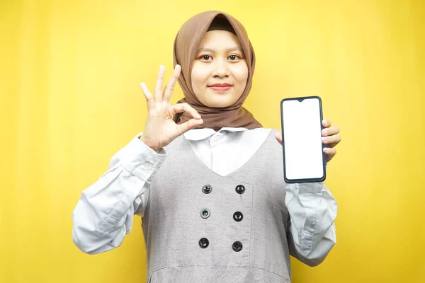美丽的年轻亚洲穆斯林女子面带微笑 充满热情和欢乐 手拿着智能手机 推销某事 手拉着应用程序 被黄色背景隔离 做广告概念 — 图库照片