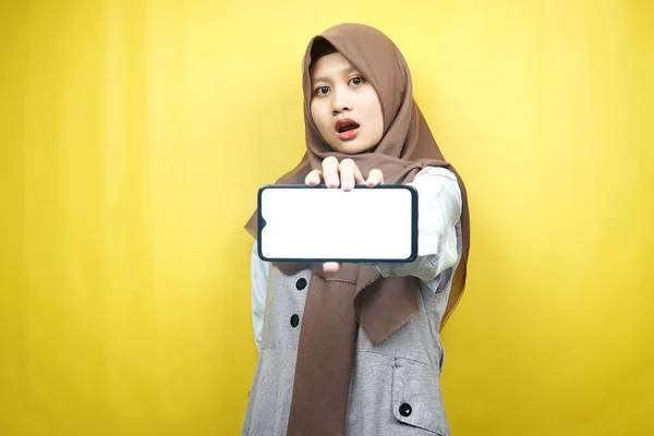 美しい若いアジアのイスラム教徒の女性はショックを受け すごい表情 空白の画面でスマートフォンを手に持ち アプリを宣伝し 製品を宣伝し 何かを提示し 黄色の背景に隔離された — ストック写真