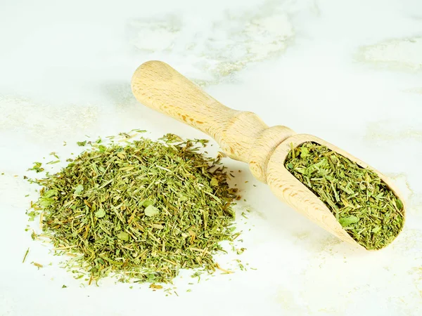 Dried parsley and dill in a wooden scoop and a handful of spices nearby