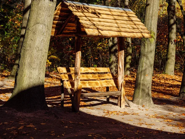 秋の公園内に木の幹の間に木製の屋根のベンチ — ストック写真