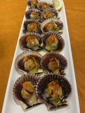 Kabuğunda ızgara deniz tarağı var, masada servis ediliyor. Zeytinyağı, sarımsak, maydanoz ve tuz ekledim. Galiçya Restoranı