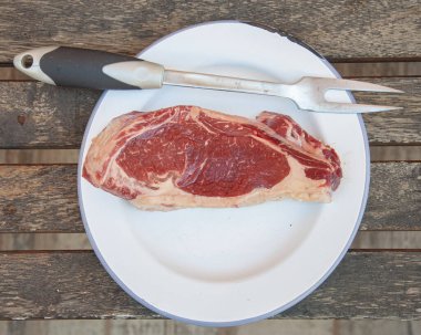 Raw prime meat steak on white plate wooden board copy space